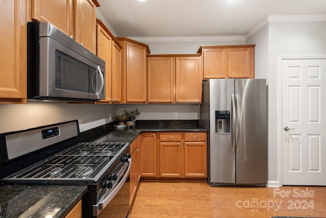 kitchen featuring light wood-type flooring, crown molding, appliances with stainless steel finishes, and dark stone counters