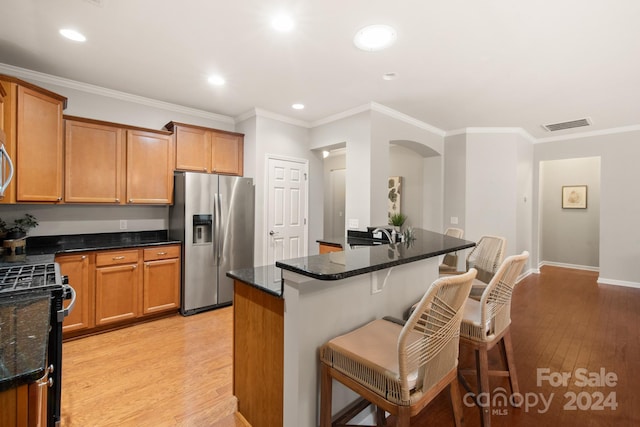 kitchen featuring dark stone counters, stainless steel fridge with ice dispenser, black stove, and light hardwood / wood-style floors