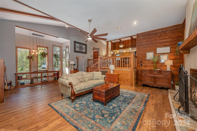 living room with hardwood / wood-style floors, ceiling fan with notable chandelier, high vaulted ceiling, and wooden walls