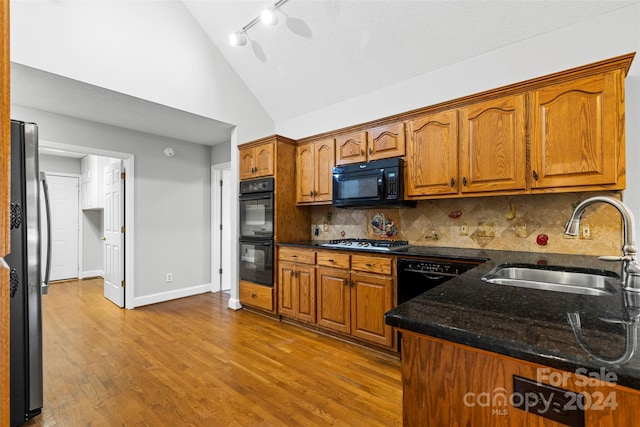 kitchen featuring backsplash, high vaulted ceiling, light wood-type flooring, black appliances, and sink