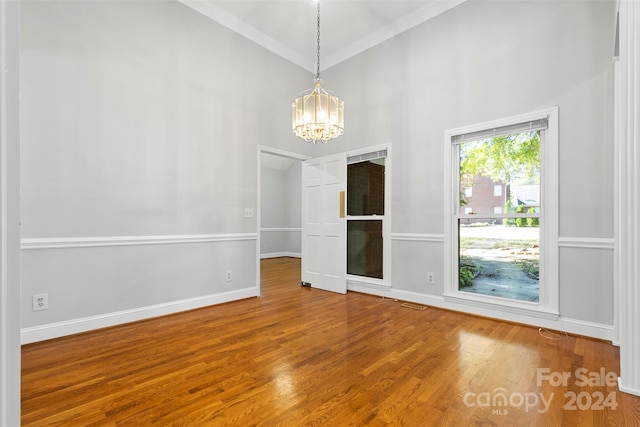 empty room featuring a notable chandelier, crown molding, hardwood / wood-style flooring, and a high ceiling