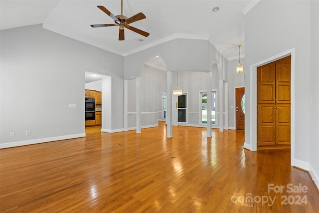 unfurnished living room with hardwood / wood-style floors, crown molding, decorative columns, high vaulted ceiling, and ceiling fan with notable chandelier