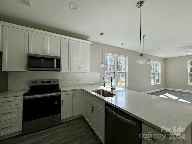 kitchen featuring appliances with stainless steel finishes, sink, kitchen peninsula, decorative light fixtures, and light stone counters