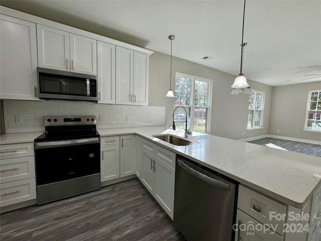 kitchen with appliances with stainless steel finishes, sink, kitchen peninsula, white cabinetry, and decorative light fixtures