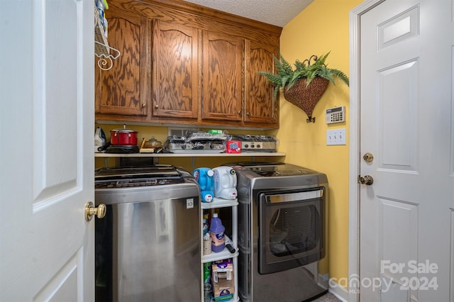 clothes washing area featuring washer and clothes dryer, a textured ceiling, and cabinets