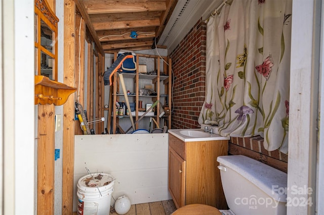 bathroom featuring toilet, vanity, brick wall, and wood-type flooring