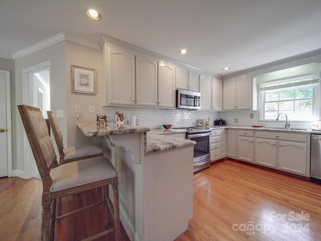 kitchen with sink, white cabinets, appliances with stainless steel finishes, light stone counters, and light hardwood / wood-style floors