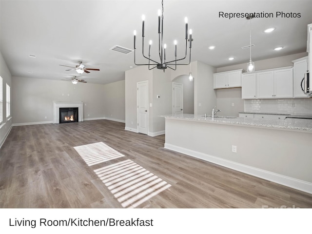 kitchen with pendant lighting, sink, light wood-type flooring, light stone countertops, and white cabinetry