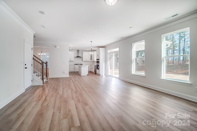 unfurnished living room with light wood-type flooring, crown molding, and a notable chandelier