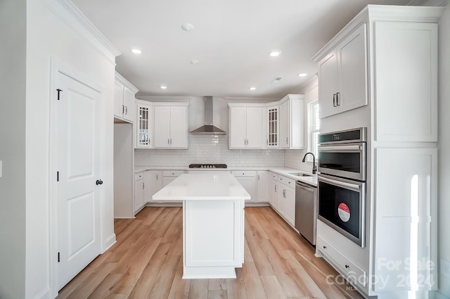 kitchen featuring wall chimney exhaust hood, a kitchen island, light wood-type flooring, and appliances with stainless steel finishes