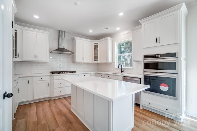 kitchen with white cabinets, wall chimney range hood, and light hardwood / wood-style flooring