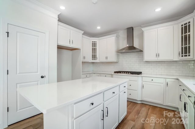 kitchen with light wood-type flooring, white cabinetry, a kitchen island, and wall chimney exhaust hood