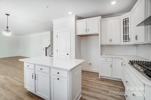 kitchen featuring white cabinets, decorative backsplash, hanging light fixtures, and light hardwood / wood-style flooring