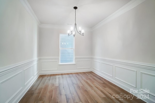 empty room with a chandelier, light hardwood / wood-style floors, and crown molding