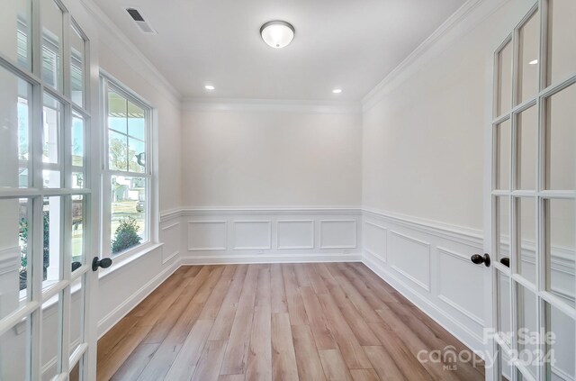 empty room with a wealth of natural light, crown molding, french doors, and light wood-type flooring