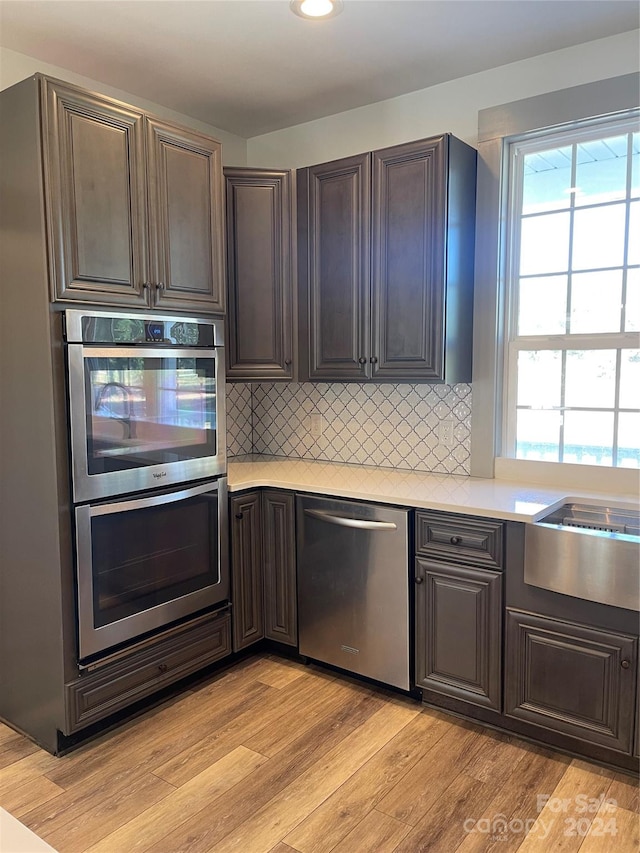 kitchen with dark brown cabinetry, stainless steel appliances, light hardwood / wood-style floors, and backsplash