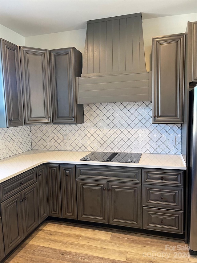 kitchen with light wood-type flooring, black electric stovetop, backsplash, and custom range hood