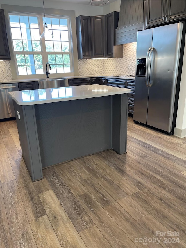 kitchen featuring stainless steel appliances, light wood-type flooring, pendant lighting, decorative backsplash, and sink