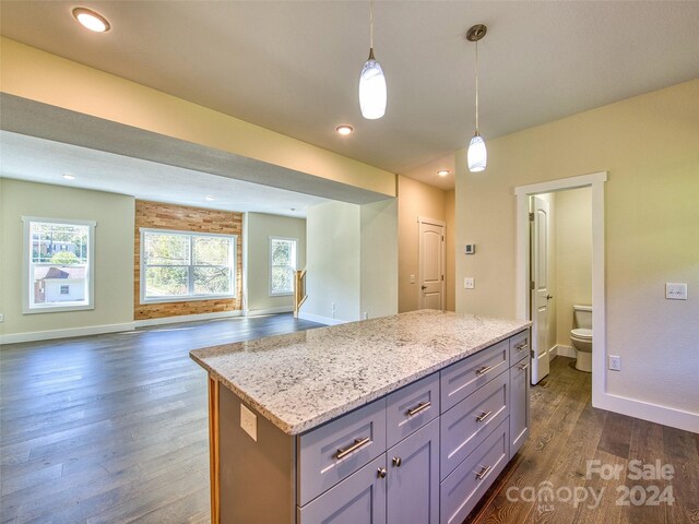 kitchen with light stone counters, dark hardwood / wood-style floors, gray cabinets, decorative light fixtures, and a center island