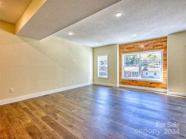 spare room with a textured ceiling, dark hardwood / wood-style floors, and wood walls