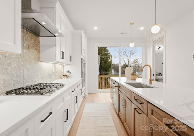 kitchen with sink, white cabinets, wall chimney range hood, and stainless steel appliances