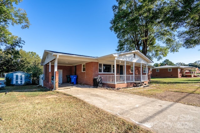 single story home with covered porch, a front yard, a carport, and a storage shed