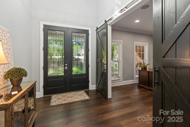 entryway featuring a barn door, french doors, dark wood-type flooring, and ornamental molding