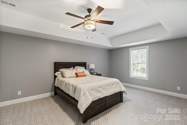 bedroom featuring light carpet, ceiling fan, and a tray ceiling