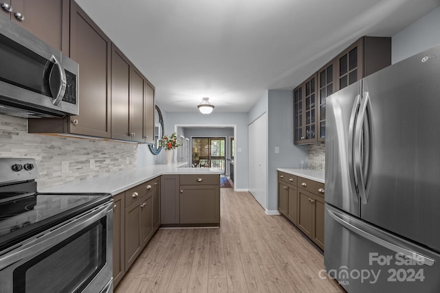 kitchen with kitchen peninsula, stainless steel appliances, decorative backsplash, and light wood-type flooring