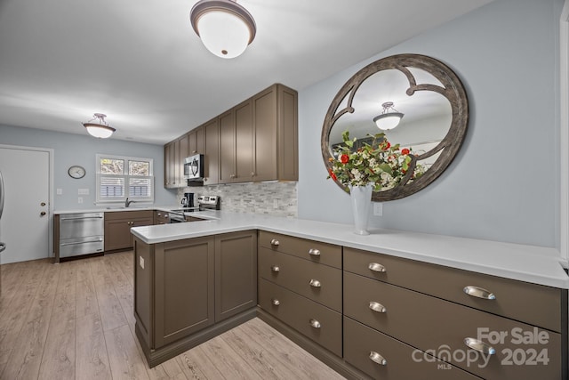 kitchen featuring sink, kitchen peninsula, light hardwood / wood-style floors, stainless steel appliances, and decorative backsplash