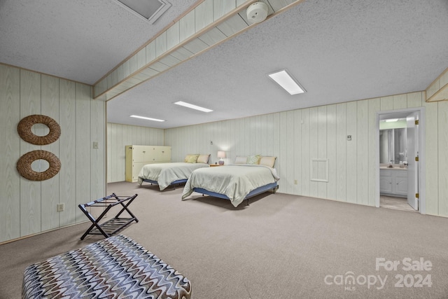 bedroom featuring light carpet, wood walls, a textured ceiling, and ensuite bathroom