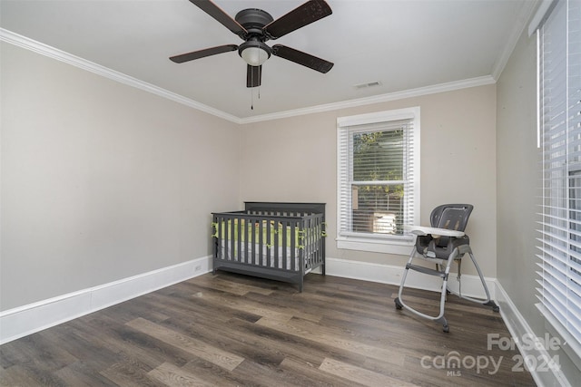 bedroom with crown molding, a crib, dark wood-type flooring, and ceiling fan