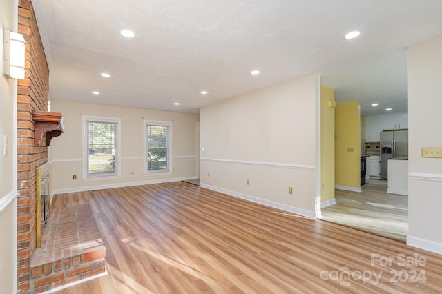 unfurnished living room with light hardwood / wood-style flooring, a textured ceiling, and a fireplace