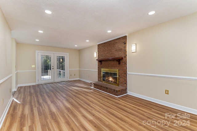 unfurnished living room with light hardwood / wood-style flooring, french doors, a textured ceiling, and a brick fireplace