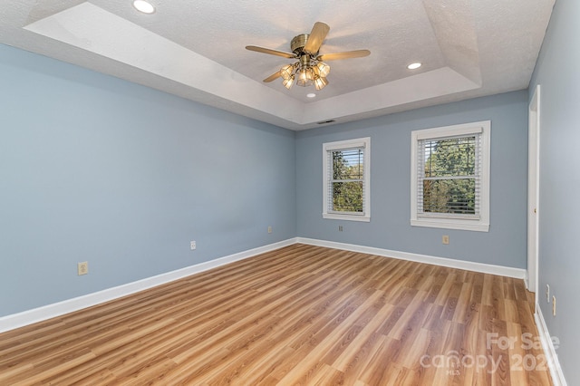 spare room with ceiling fan, a raised ceiling, a textured ceiling, and light wood-type flooring