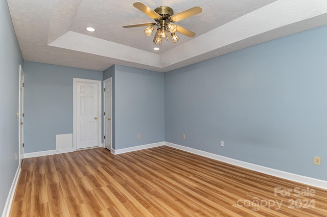 spare room with a textured ceiling, light hardwood / wood-style flooring, a tray ceiling, and ceiling fan