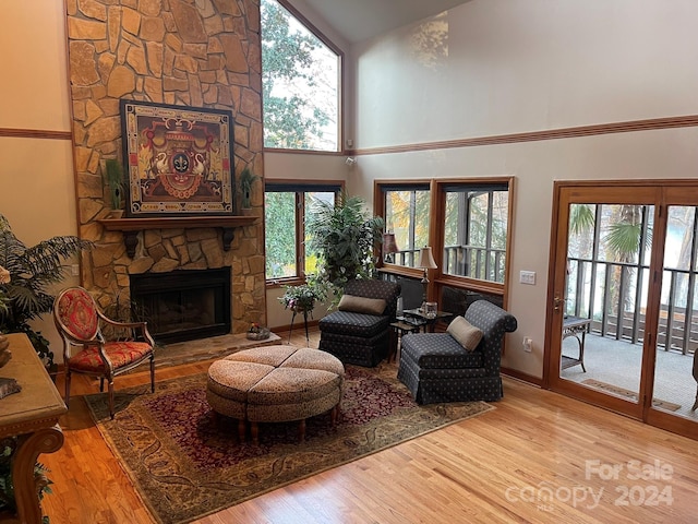 living room with a stone fireplace, plenty of natural light, high vaulted ceiling, and light wood-type flooring