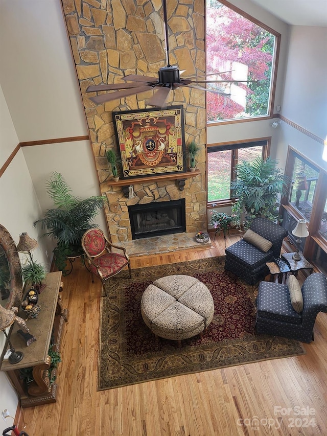 living room with a stone fireplace, ceiling fan, high vaulted ceiling, and hardwood / wood-style flooring