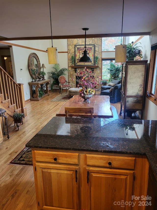 kitchen featuring light hardwood / wood-style flooring, dark stone countertops, crown molding, pendant lighting, and a fireplace