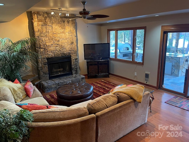 living room featuring wood-type flooring, heating unit, a stone fireplace, and ceiling fan