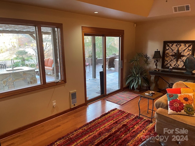 doorway to outside with heating unit, sink, lofted ceiling, and hardwood / wood-style flooring