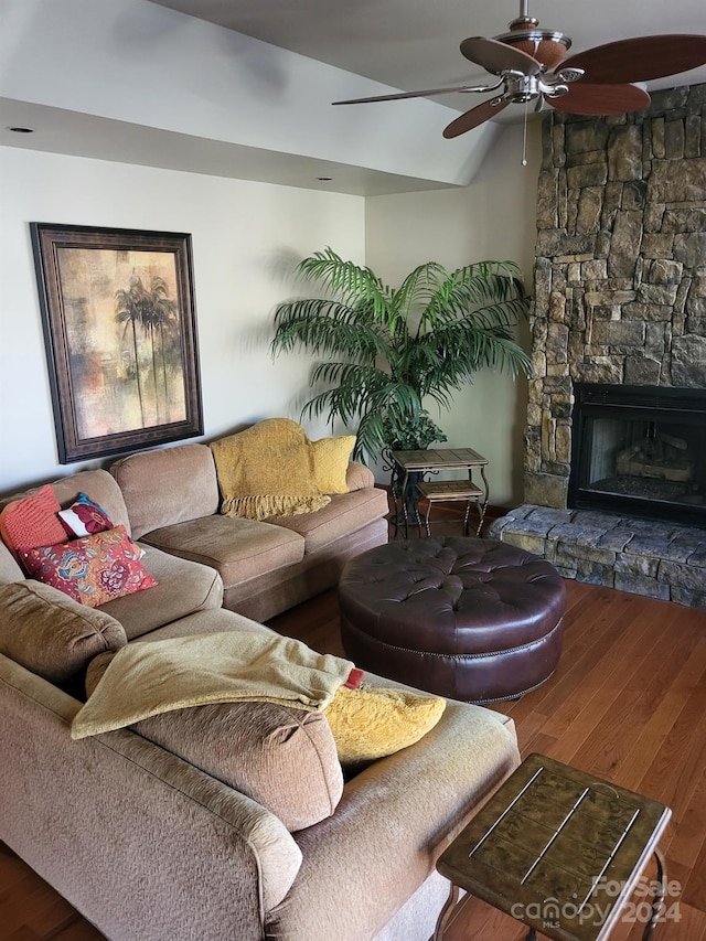 living room featuring ceiling fan, a stone fireplace, wood-type flooring, and vaulted ceiling