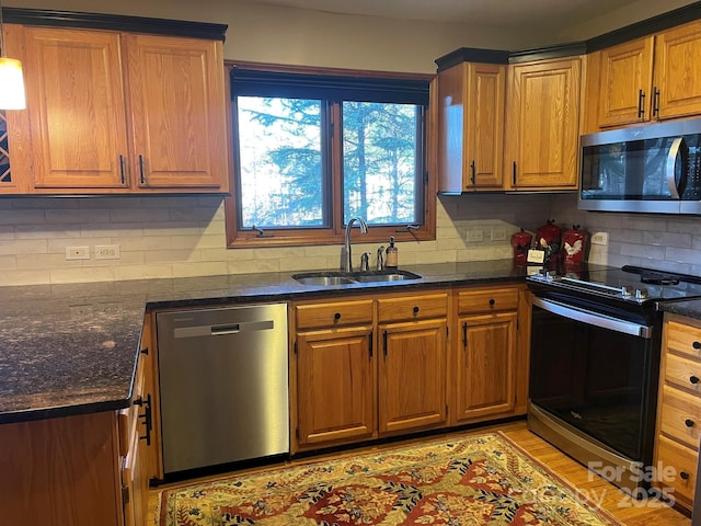 kitchen featuring decorative backsplash, appliances with stainless steel finishes, brown cabinets, dark stone countertops, and a sink