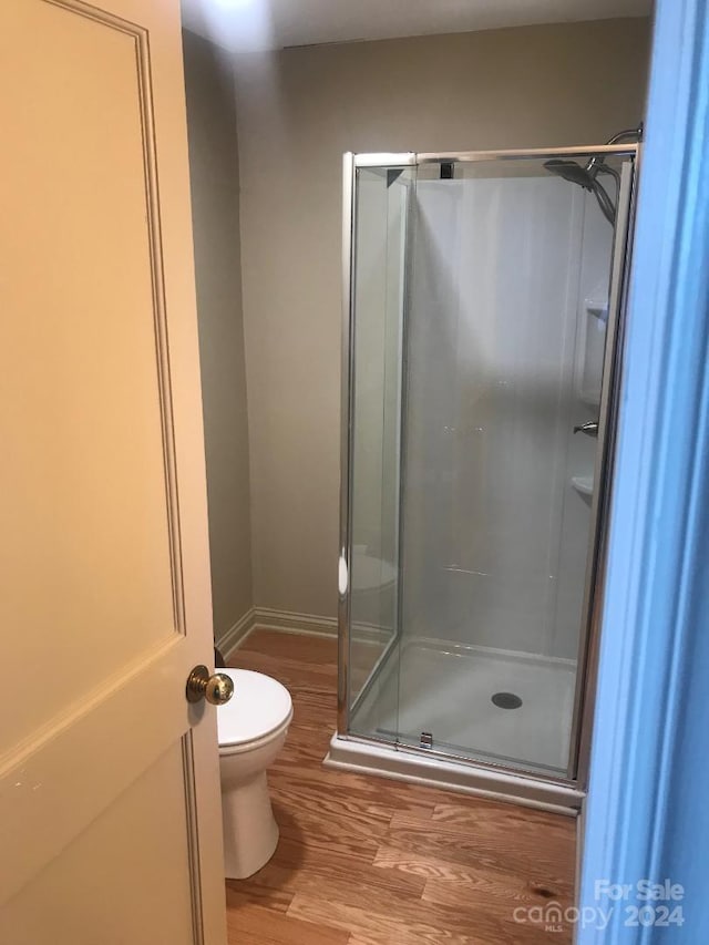 bathroom with hardwood / wood-style floors, toilet, and a shower with door