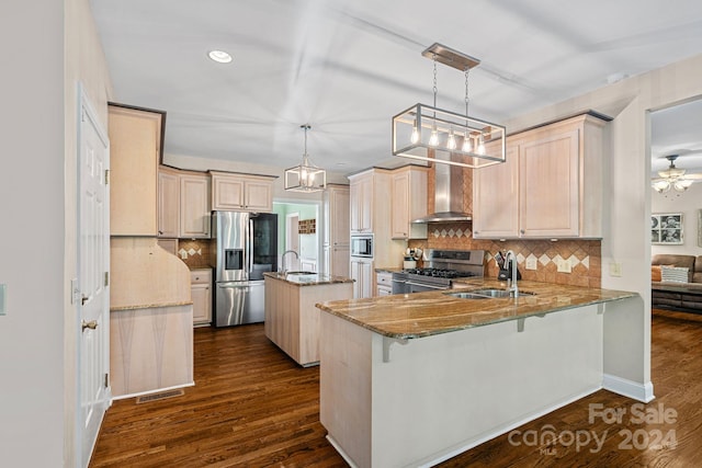 kitchen featuring wall chimney range hood, sink, appliances with stainless steel finishes, decorative light fixtures, and kitchen peninsula