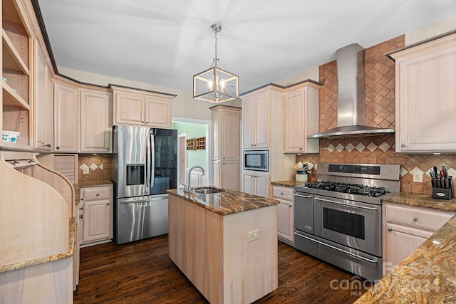 kitchen with stainless steel appliances, sink, wall chimney range hood, a center island with sink, and hanging light fixtures