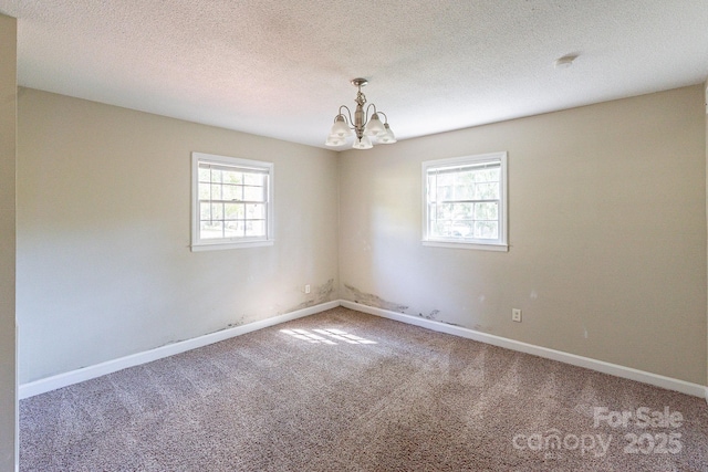 empty room featuring carpet floors, a notable chandelier, baseboards, and a textured ceiling