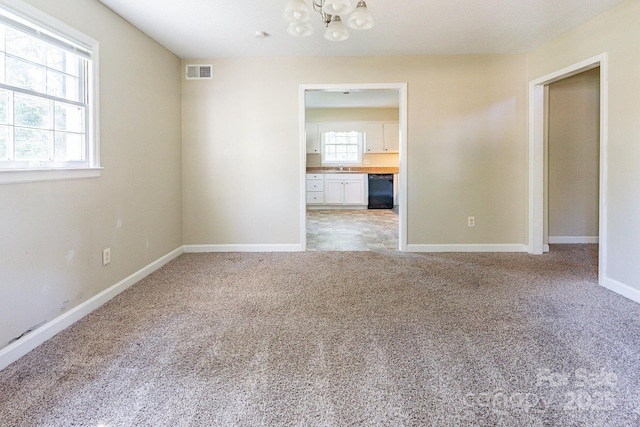 spare room featuring a notable chandelier, visible vents, light carpet, a sink, and baseboards