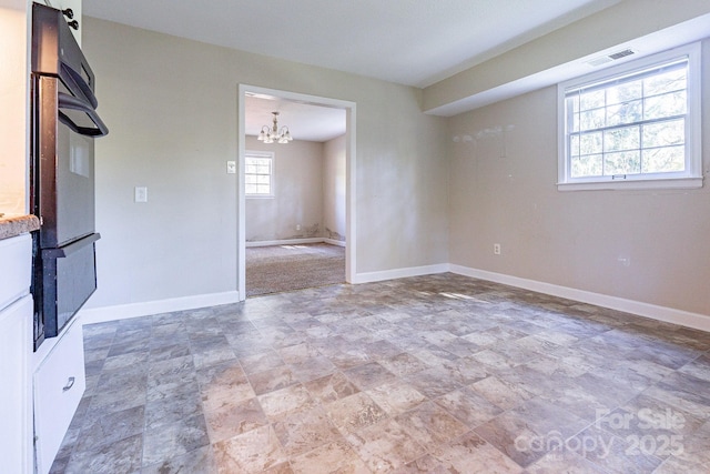 unfurnished room featuring a notable chandelier, visible vents, and baseboards