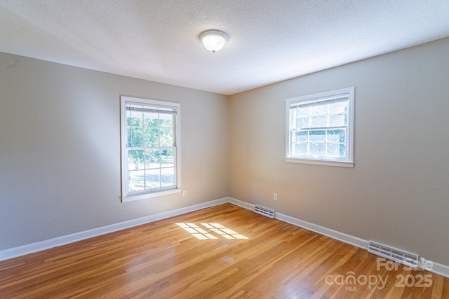 empty room with light wood-type flooring, visible vents, a textured ceiling, and baseboards